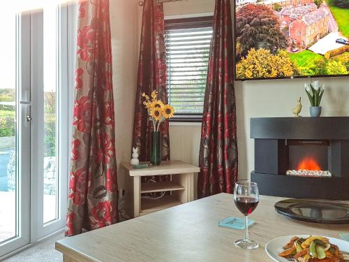 a table with a glass of wine and a fireplace at Forrest Lodge in Plumbland