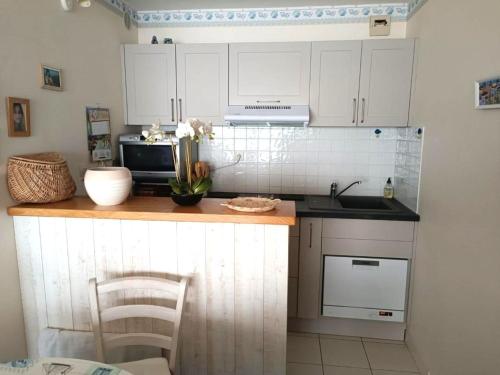 une cuisine avec des placards blancs et un comptoir avec des fleurs. dans l'établissement Studio face à la mer avec balcon, garage privé et équipements modernes - Les Sables-d'Olonne - FR-1-92-624, à Les Sables-dʼOlonne