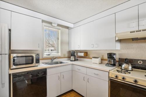 Una cocina con gabinetes blancos, un fregadero y un microondas. en Village Green 8D, en Stowe
