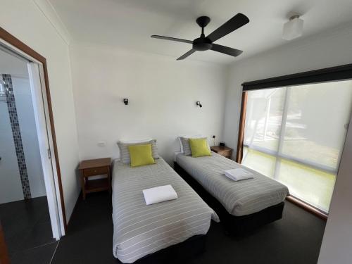 two beds in a room with a ceiling fan at Prom Coast Holiday Lodge in Waratah Bay