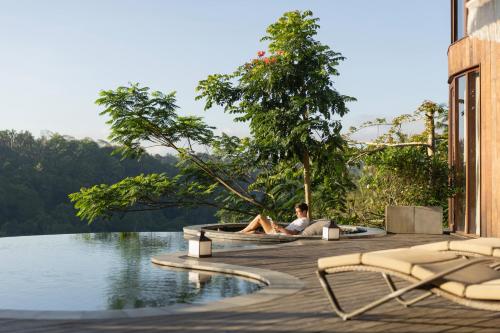 a man sitting on a deck next to a body of water at Akohara Buahan Village Retreat in Payangan