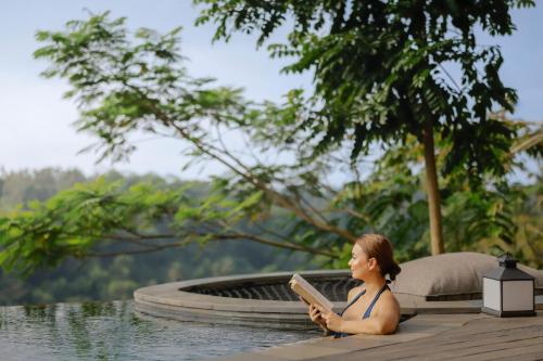 a woman reading a book in a swimming pool at Akohara Buahan Village Retreat in Payangan