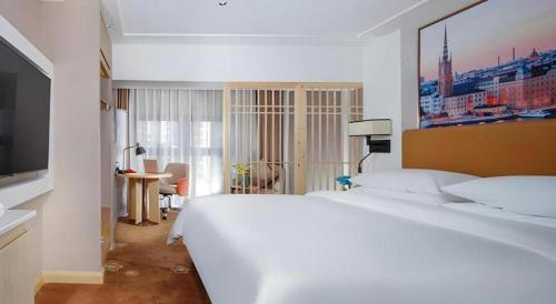 a white bedroom with a large bed and a television at Vienna Hotel Chengdu Exhibition Center In Time City in Chengdu