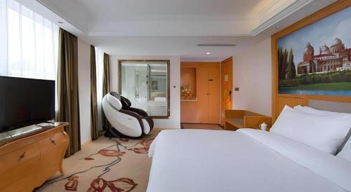 a bedroom with a bed and a chair and a television at Vienna Hotel Hubei Jinzhou Changjiang University in Caoshi