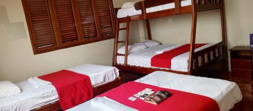 a room with three bunk beds with red and white sheets at Hostal Dalimar in Salinas