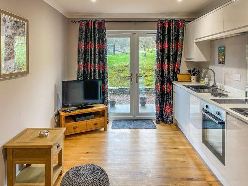 cocina con TV y mesa y cocina con cortinas en Dalnafeidh Beag - Cottage, en Portnacroish