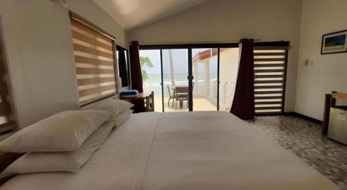 a bedroom with a large white bed and a balcony at Coral Beach Club in Matabungkay