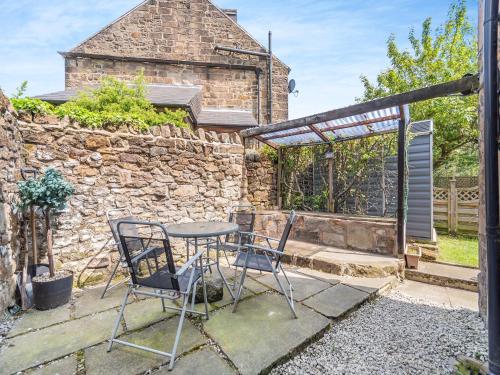 a patio with a table and chairs and a stone wall at River Cottage in Two Dales