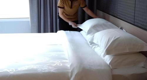 a man standing next to a bed with pillows at Hanyong Hotel Shenzhen International Exhibition Center in Shenzhen