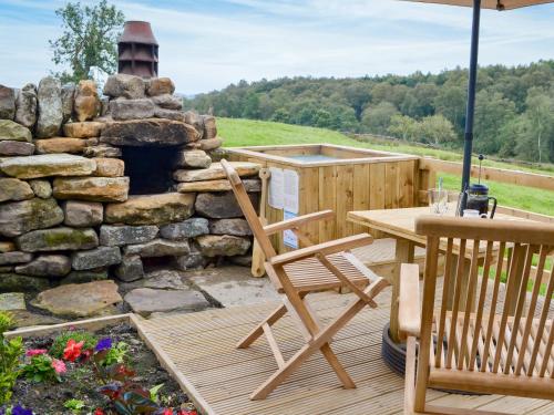 a deck with a table and chairs and a stone fireplace at The Old Back Kitchen At Bonfield Ghyll Farm in Chop Gate