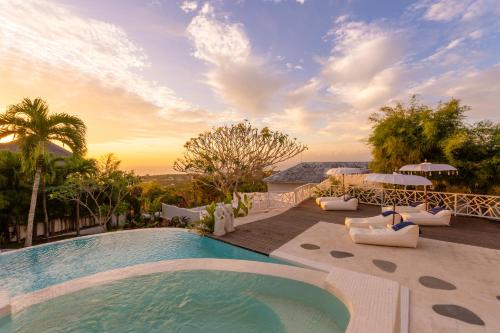 a pool with chairs and a sunset in the background at Gravity Boutique Suites in Uluwatu