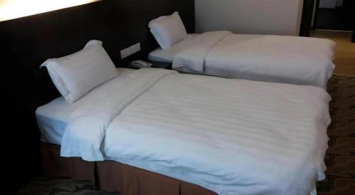 two beds in a hotel room with white sheets and pillows at Eminent Hotel in Kota Kinabalu