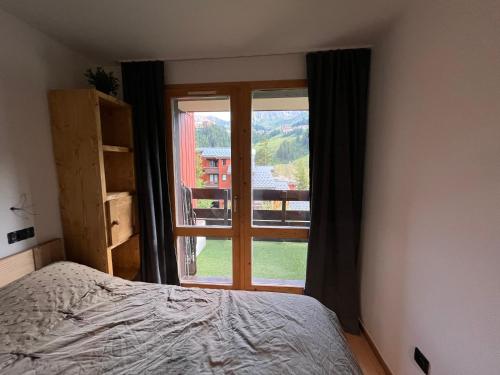 une chambre avec un lit et une grande fenêtre dans l'établissement Appartement LA PLAGNE plein sud au pied des pistes, piscine et parking gratuits, à La Plagne Tarentaise