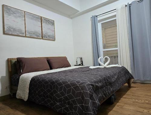 a bedroom with a bed with a black comforter and a window at Island Escape Mactan Cebu Amani Grand Residences in Pusok