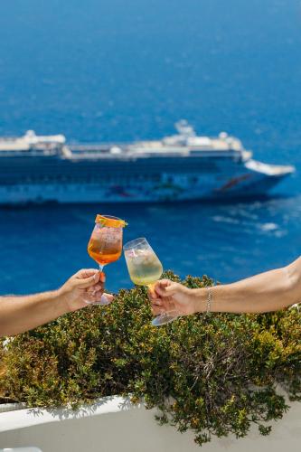 two people holding wine glasses with a cruise ship in the background at Kastro Suites in Fira