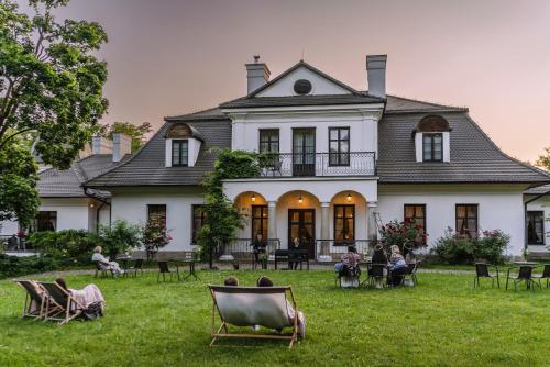 a group of people sitting in chairs in front of a house at Dwór Kombornia - Folwark in Kombornia