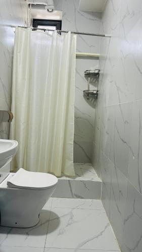 a white bathroom with a shower curtain and a toilet at Deutsch Hostel Osh in Osh