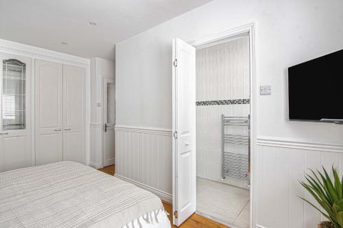 a white bedroom with a bed and a flat screen tv at The Roost Group - Brands Hatch 6 Bedroom Home in Fawkham