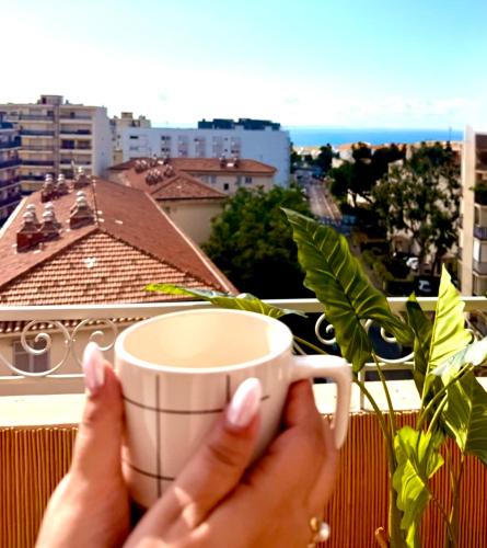 a person holding a cup of coffee on a balcony at Votre grand COCON Nicois in Nice