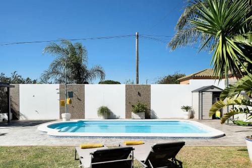 a swimming pool in a yard with two chairs and a palm tree at Villa con piscina privada terraza privada in Conil de la Frontera