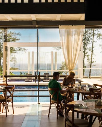 two people sitting at tables in a restaurant with a pool at Greco Hotel in Búzios