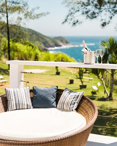 a wicker chair with pillows and a table with wine glasses at Greco Hotel in Búzios