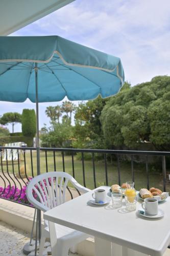 une table blanche avec un parasol bleu et de la nourriture dans l'établissement MOTEL ASCOT - Hotel & Appartements, à Cagnes-sur-Mer