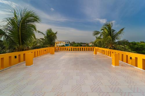 a balcony with a yellow railing and palm trees at Neithal Farm Resort with Swimming Pool by Roscotel in Puducherry