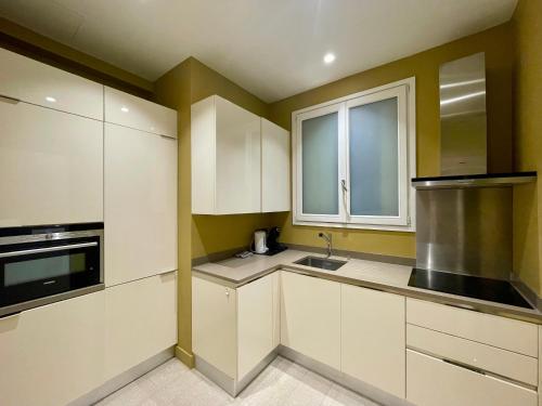 une cuisine avec des armoires blanches, un évier et une fenêtre dans l'établissement Appartement Tour Eiffel Montaigne, à Paris