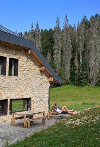 a woman sitting on a picnic table next to a building at La loge de la Dolarde in Prémanon