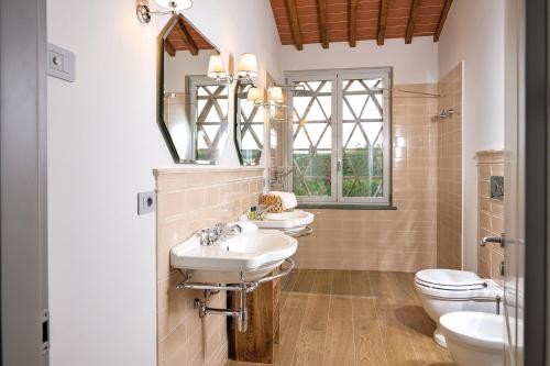 a bathroom with two sinks and a toilet and a mirror at Castello Vicchiomaggio in Greve in Chianti
