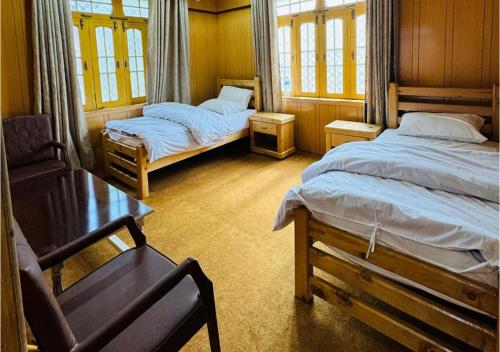 a bedroom with two beds and a chair and a table at Fatah Kin Guest House in Skardu