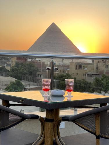 a table with two wine glasses and the pyramid at AKHNATON Pyramids View Hotel With Rooftop Access & free airport pickup in Cairo