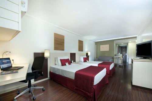 a hotel room with two beds and a desk and a computer at Comfort Suites Macaé in Macaé