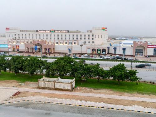 a large white building with trees in front of a street at Daar AL Maqam Suites Apartments Salalah in Salalah
