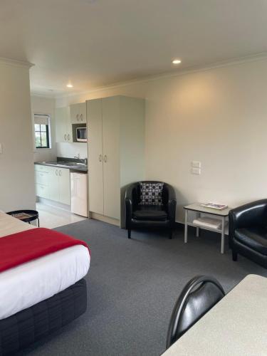 a hotel room with a bed and chairs and a kitchen at Kerry Lane Motel in Hawera