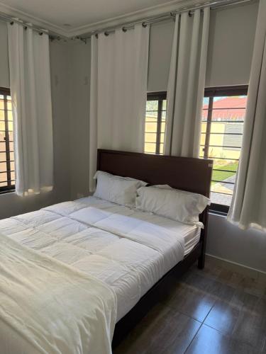 a bedroom with a bed with white sheets and windows at MY Home Apartments in Lusaka