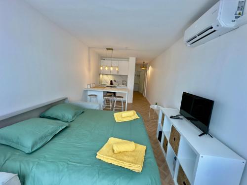 a bedroom with a green bed and a kitchen at La Casa Carnon - Sur le Port - Moderne & Lumineux in Mauguio