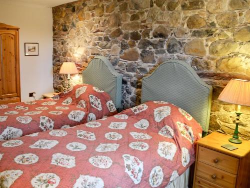 a bedroom with two beds and a stone wall at The Old Stables in Uldale