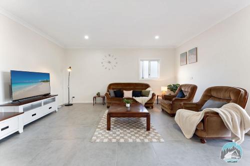 a living room with leather furniture and a flat screen tv at Spacious 4 Bedroom House Near Station & Parramatta in Guildford