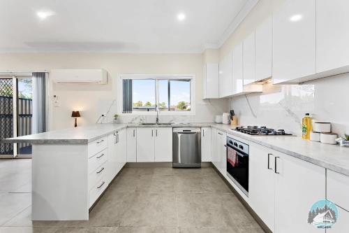 a kitchen with white cabinets and a large window at Spacious 4 Bedroom House Near Station & Parramatta in Guildford