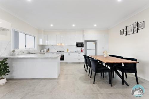 a white kitchen with a wooden table and black chairs at Spacious 4 Bedroom House Near Station & Parramatta in Guildford