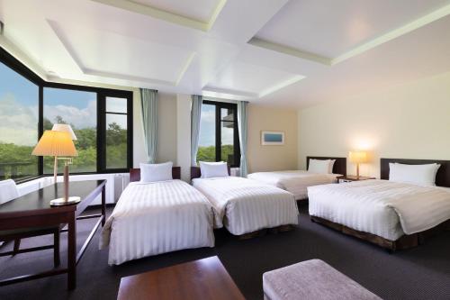 a bedroom with two beds and a desk and windows at Yatsugatake Kogen Lodge in Minamimaki