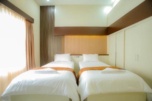 two beds in a hotel room with a window at Garuda Hotel By Calandra in Banda Aceh