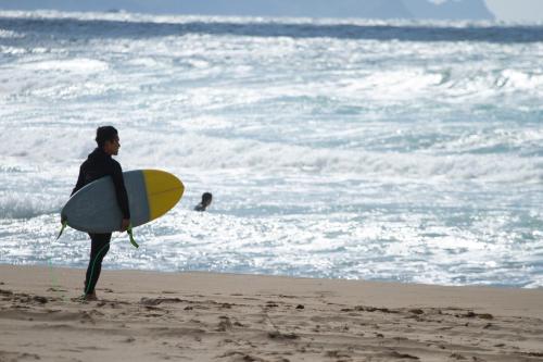 a man standing on the beach holding a surfboard at Ichiboukan Hanare Kai in Kyotango