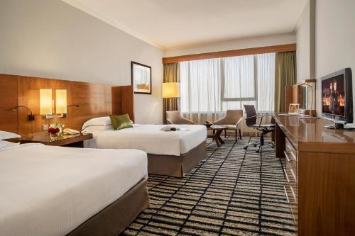 a hotel room with two beds and a desk at Jumeira Rotana – Dubai in Dubai