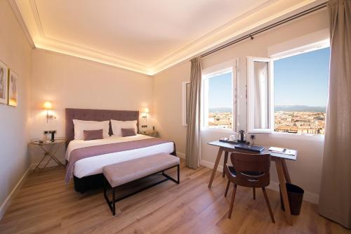 Real Segovia by Recordis Hotels في سيغوفيا: غرفة في الفندق بها سرير ومكتب ونافذة