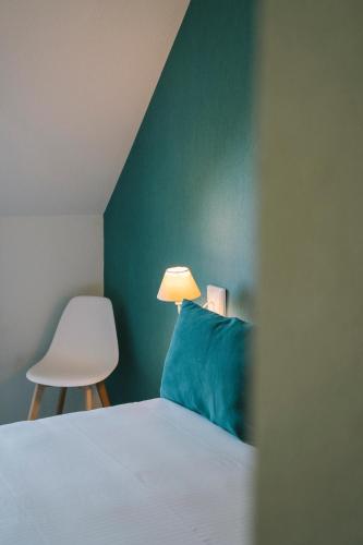 a bed with a blue pillow and a white chair at Hotel Aigue Marine in Tréguier