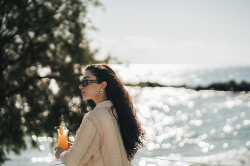 a woman walking by the water holding an orange drink at Golden Coast Suites in Kipseli