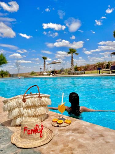a woman sitting in a swimming pool with a drink at Family Village Marrakech in Marrakech